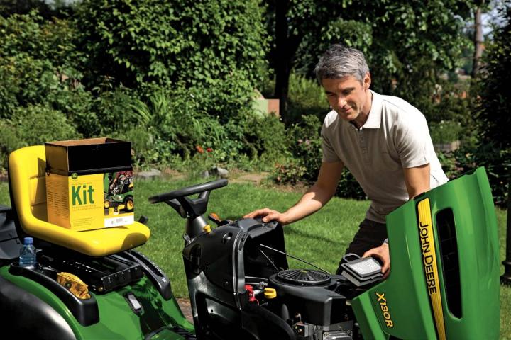 A képen egy szerelő látható, amint a John Deere ráülős fűnyírót szereli.